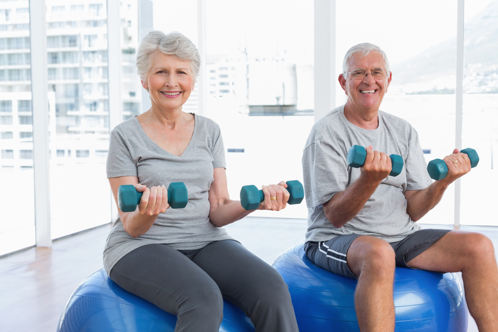 Senior couple exercising on fitness balls with dumbbells at the UAB Med West cardiac rehab.