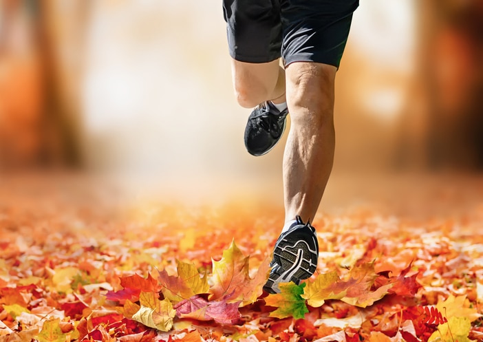 A man’s legs running through fallen red and orange leaves for fall fitness.