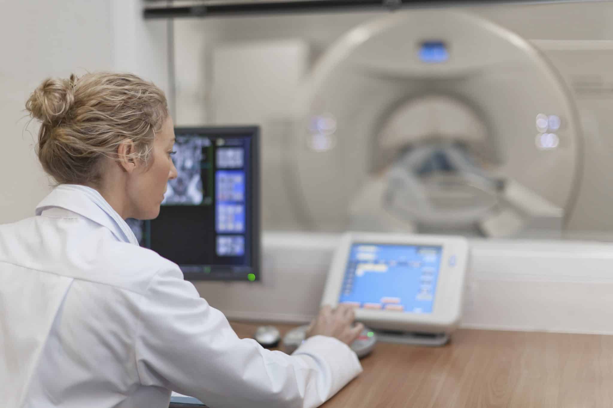 Image of a doctor working a screen outside of a tomography room.