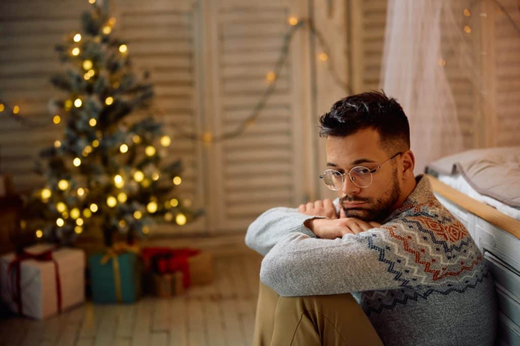 A man sitting in a room with a Christmas tree, looking contemplative.