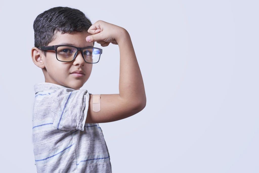 Portrait of happy healthy young kid showing bandage plaster on arm shoulder after getting vaccination.